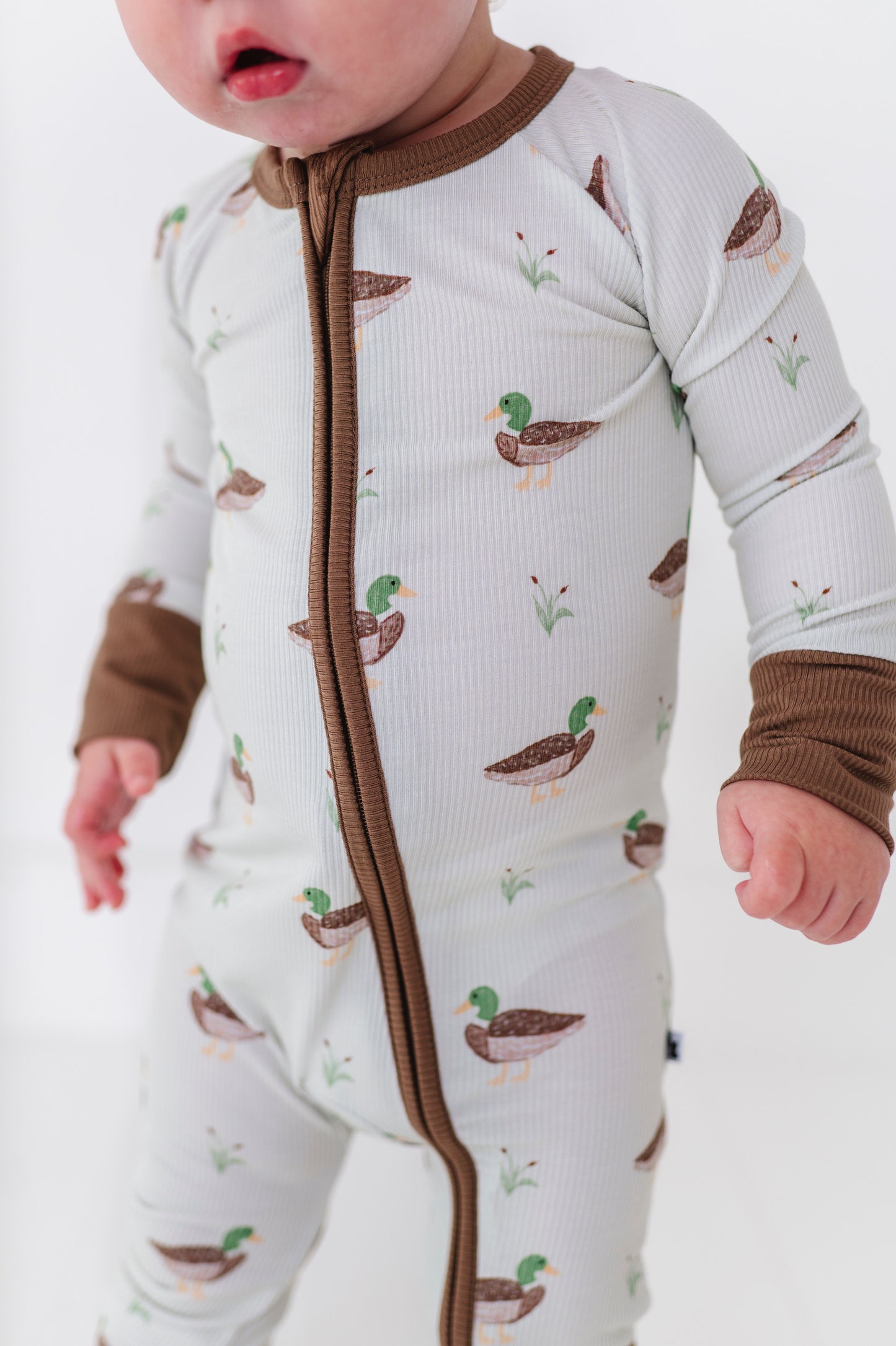 Baby in a onesie with duck pattern and brown arm bands on a white background