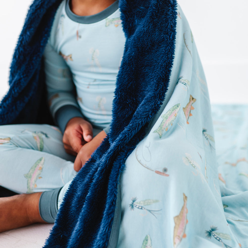 Child wrapped in a blue blanket with airplane pattern, sitting on a white surface.
