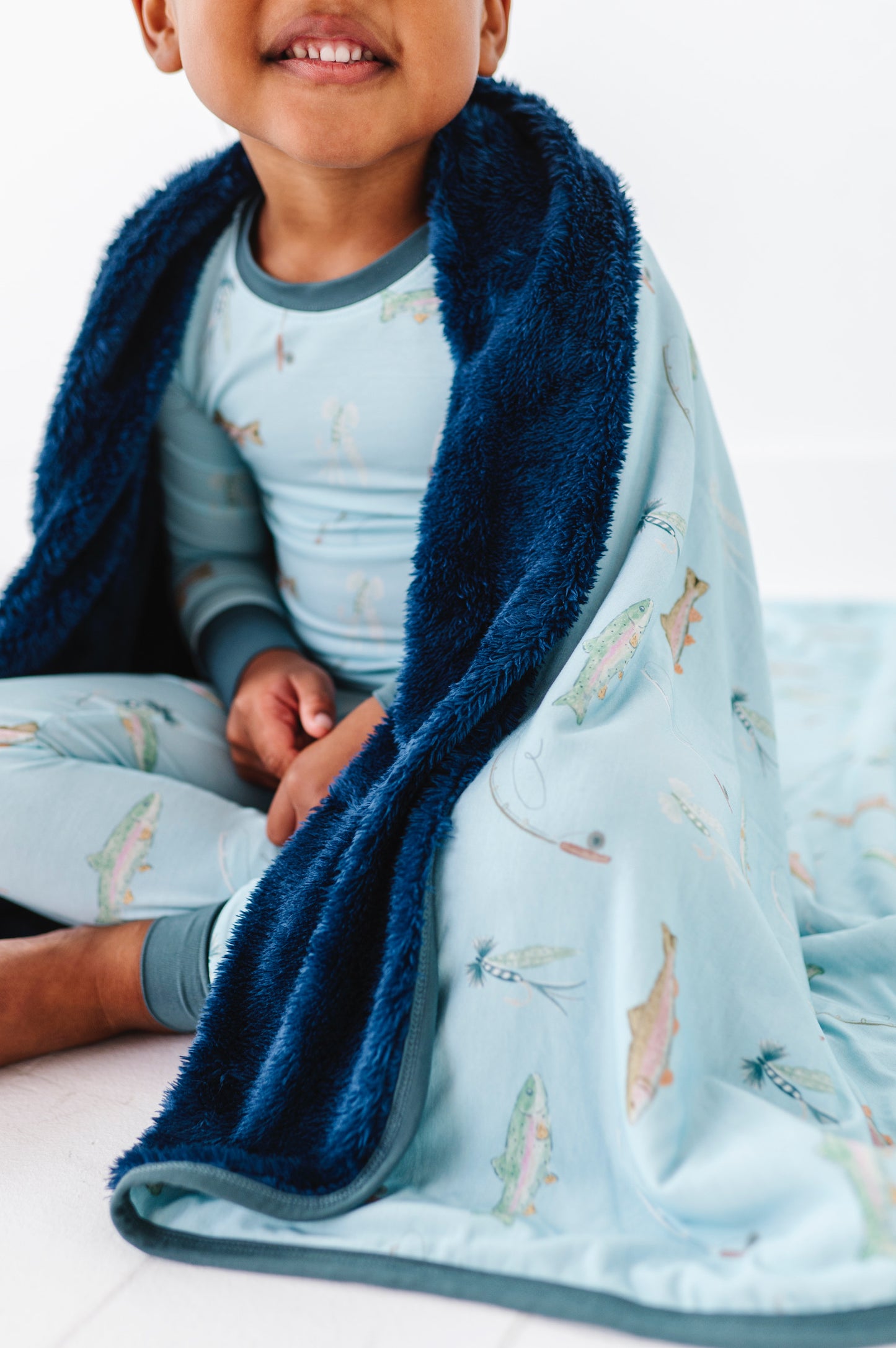 Child wrapped in a blue blanket with airplane pattern, sitting on a white surface.
